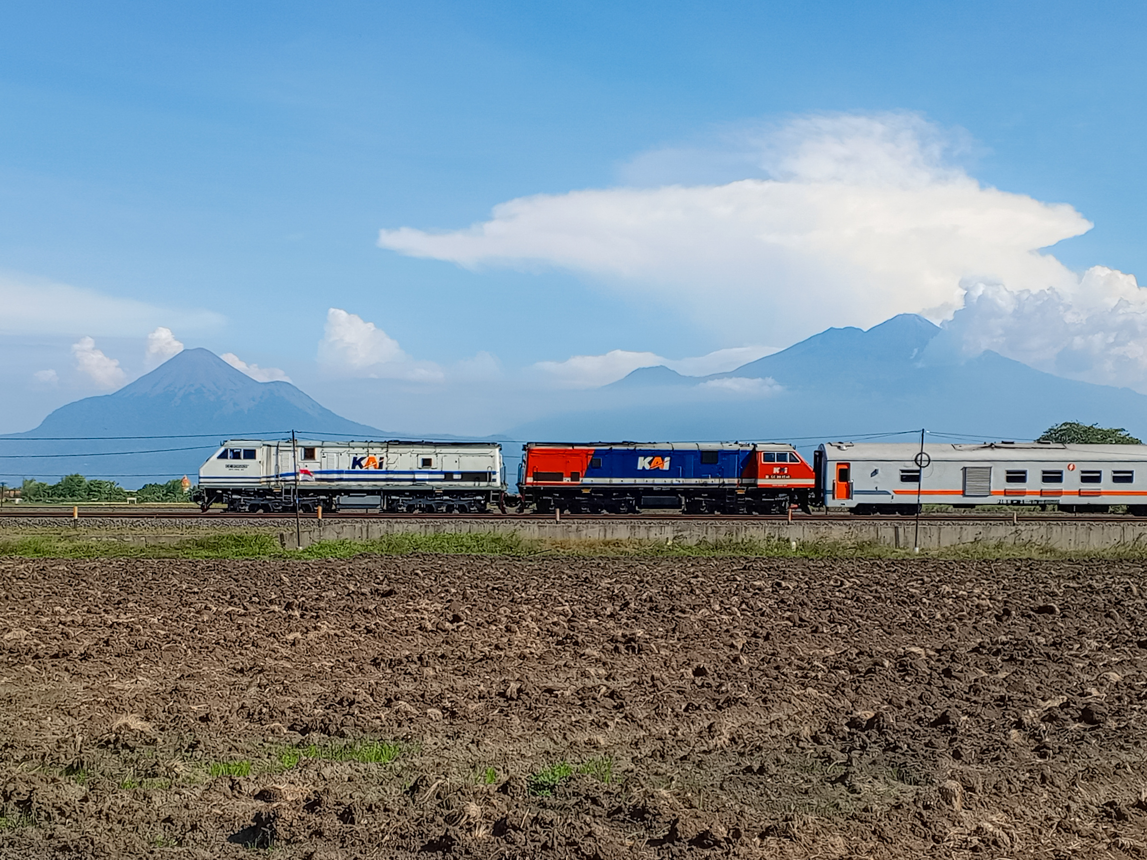 Dua Lokomotif Berjalan Berdampingan dengan background diantara dua gunung
