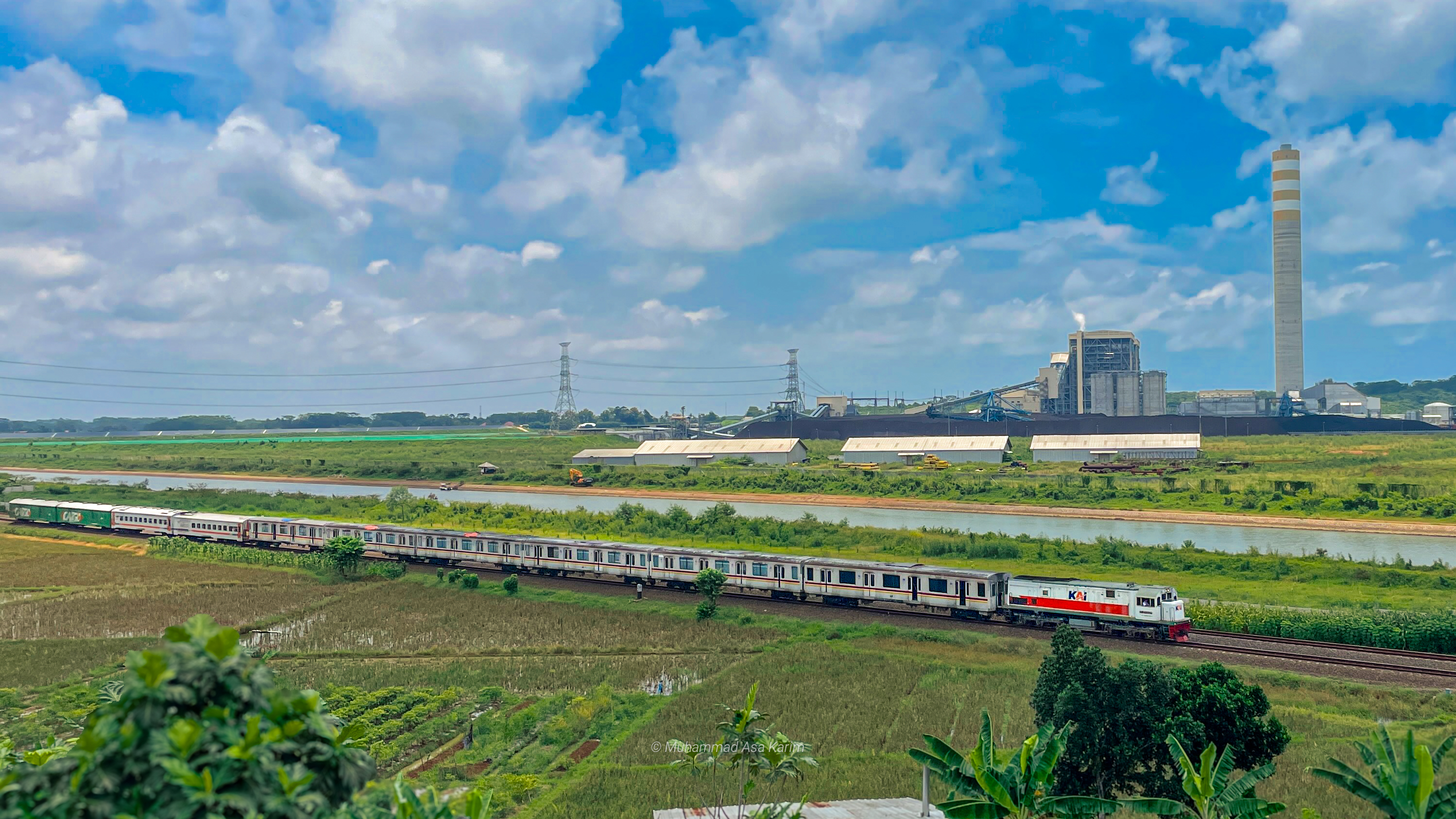 Kereta rel listrik (KRL) melaju di jalur yang berdekatan dengan pembangkit listrik, sebuah pemandangan unik di Indonesia.