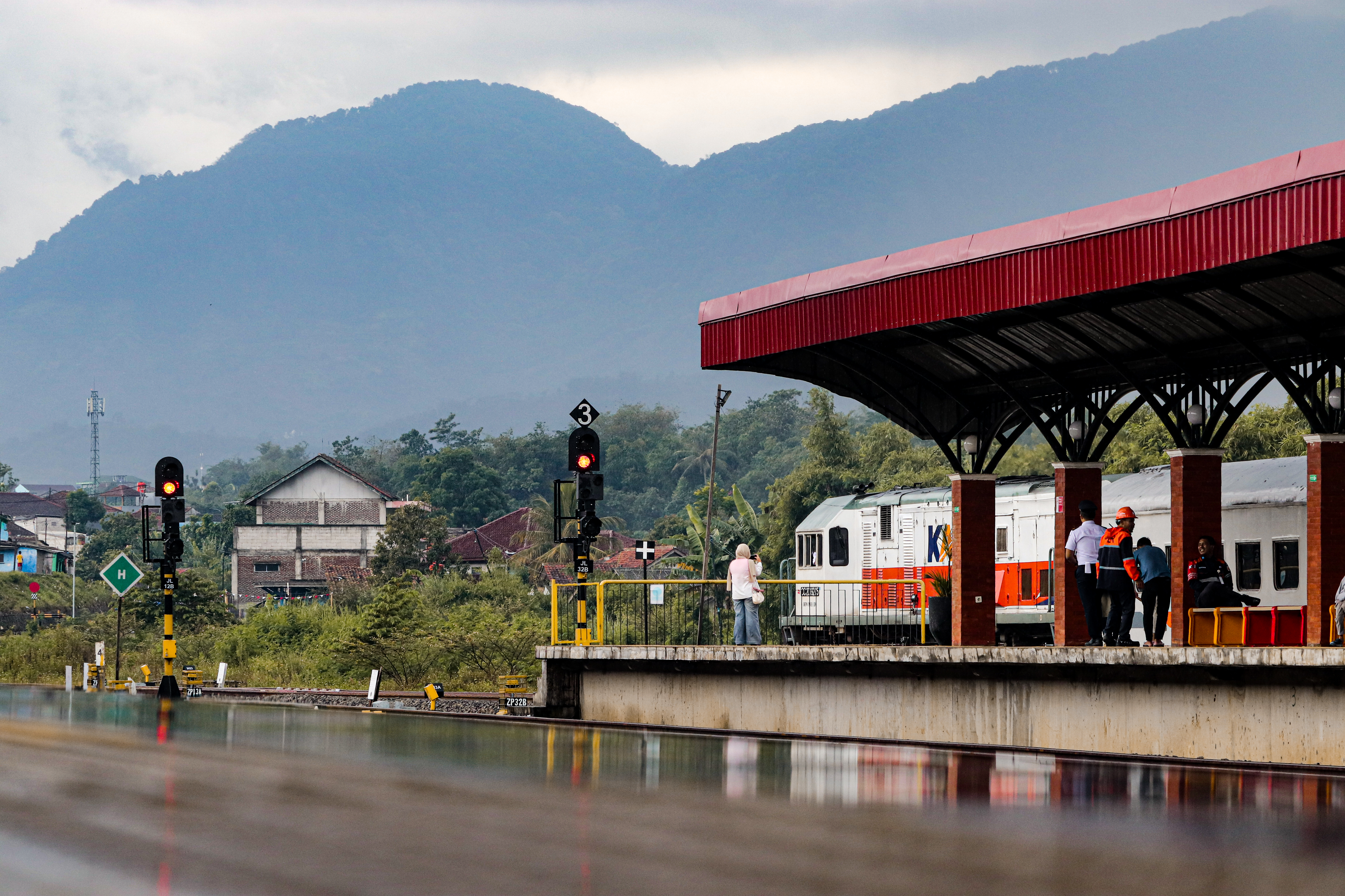Keindahan alam setelah dilanda hujan dengan objek gunung, orang, dan kereta api lokal baraya