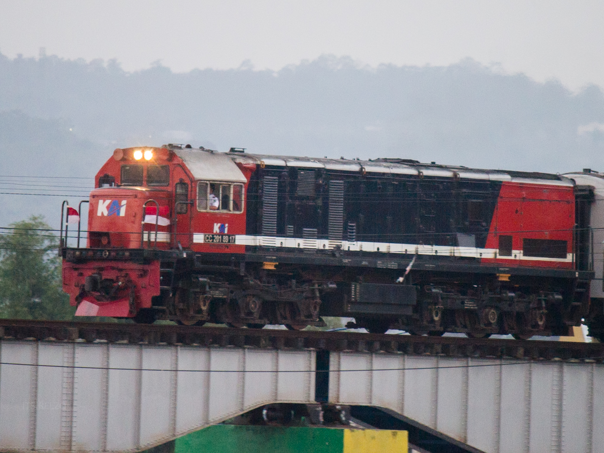 lokomotif merah yang sedang melaju di atas jembatan dengan bendera merah putih yang berkibar dengan gagah